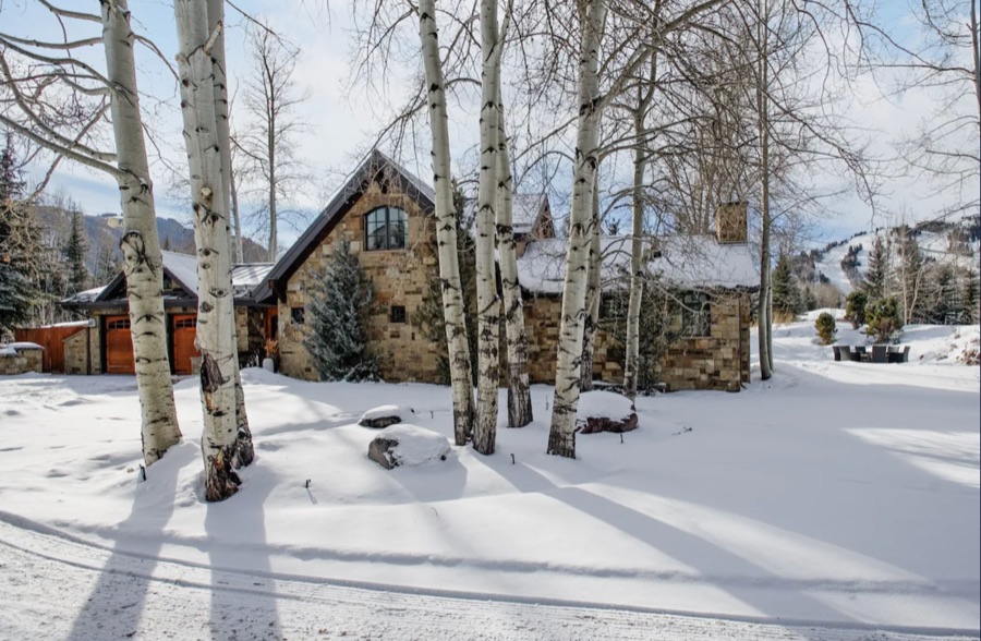 The house in winter among tall aspen trees, with the ski runs of Buttermilk on the mountain behind.