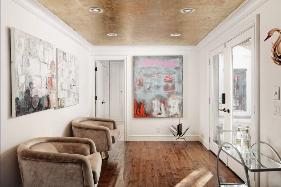 Sitting area with two velvet swivel chairs, abstract paintings, a gilded ceiling and French doors.