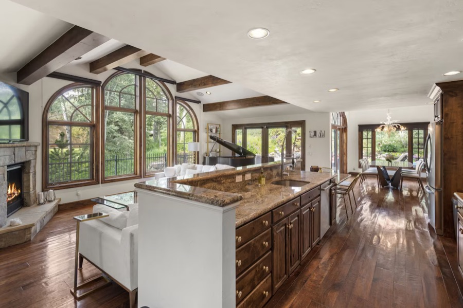 Open kitchen with granite island, dark wood cabinetry and stainless appliances, looking through to the living room in summer.